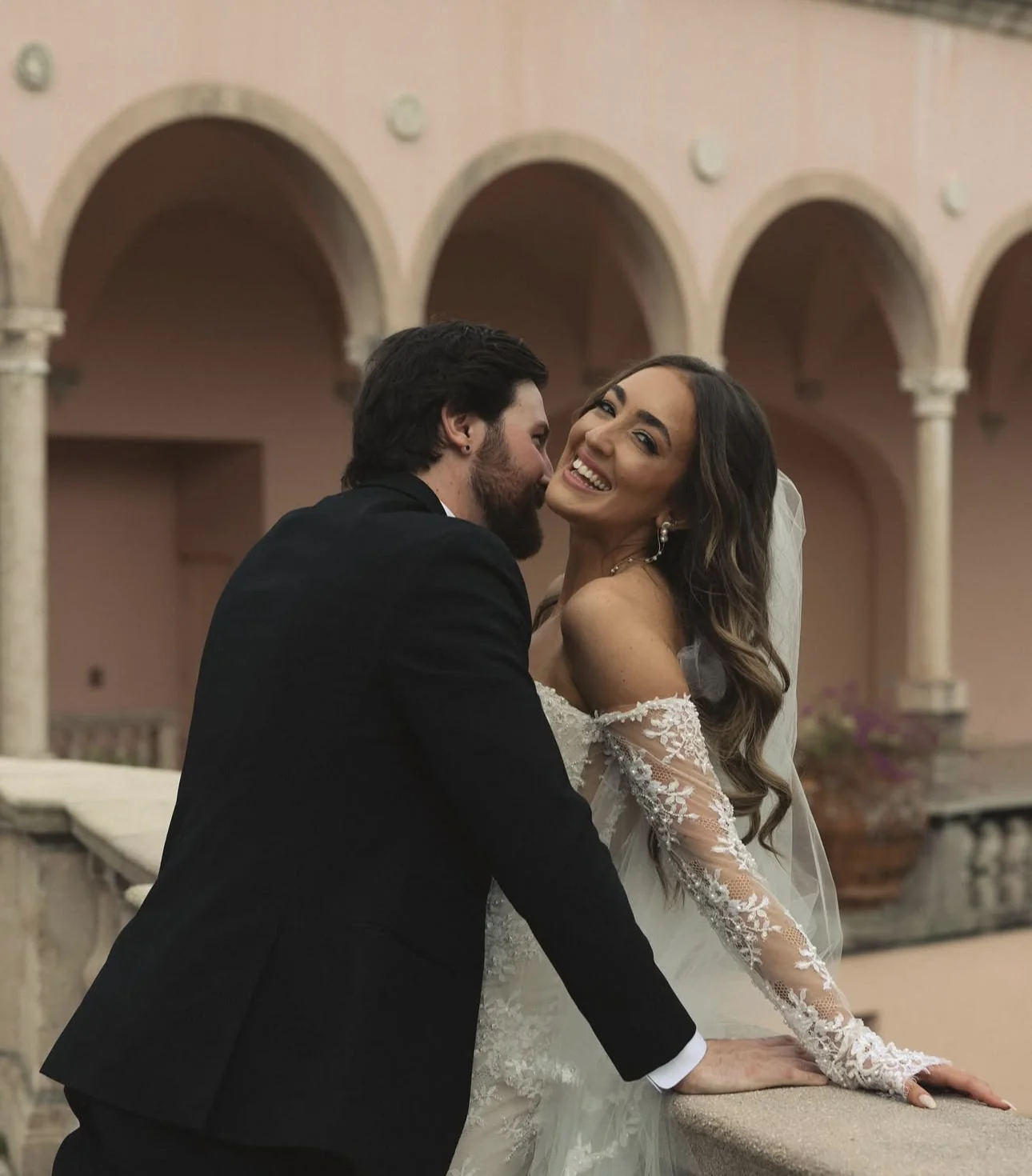 Bride and groom posing on a blush-toned balcony